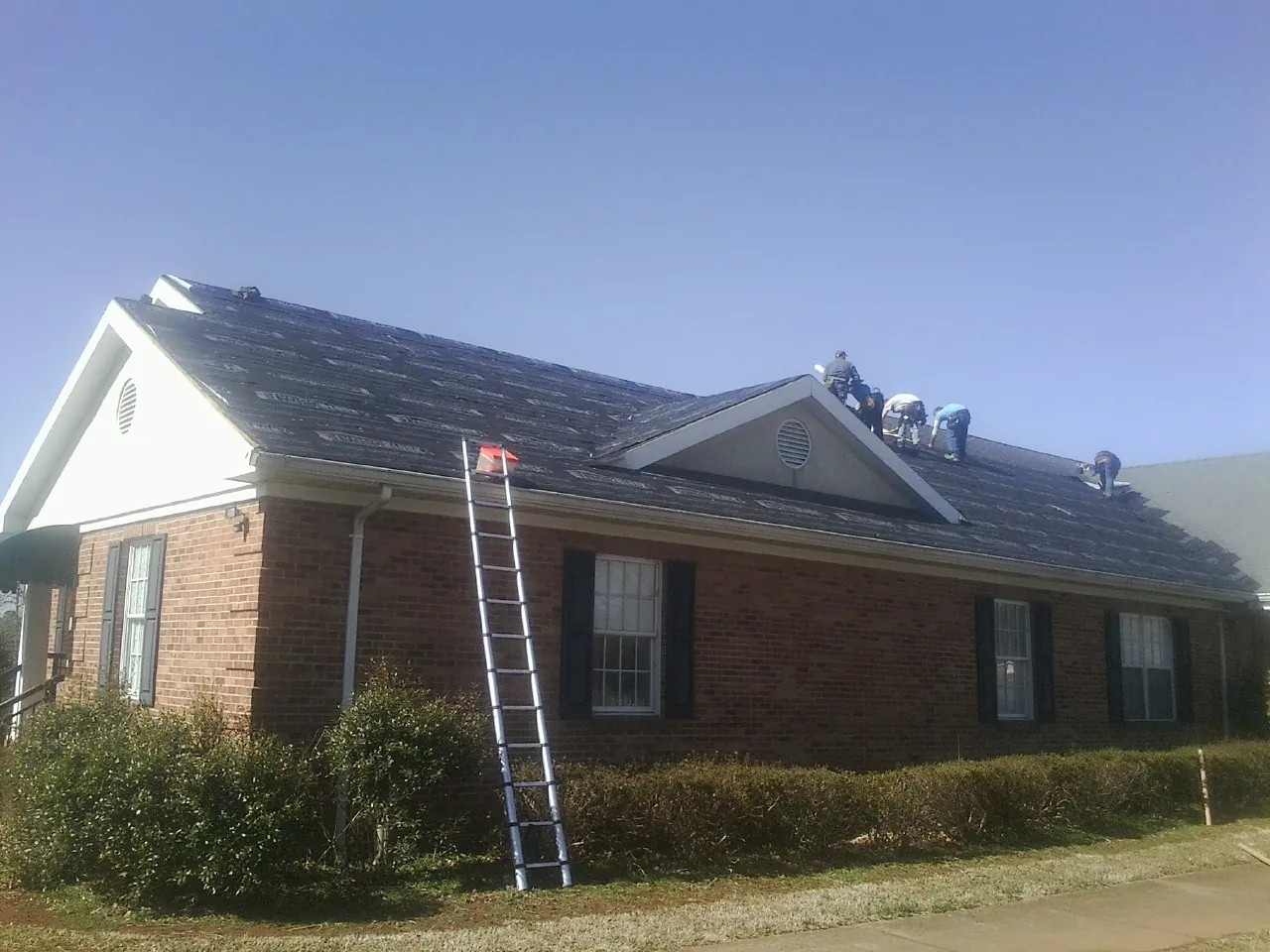 Crew tearing shingles off a brick ranch roof with a ladder set — Metal Roof Repair work by our crew in Centreville