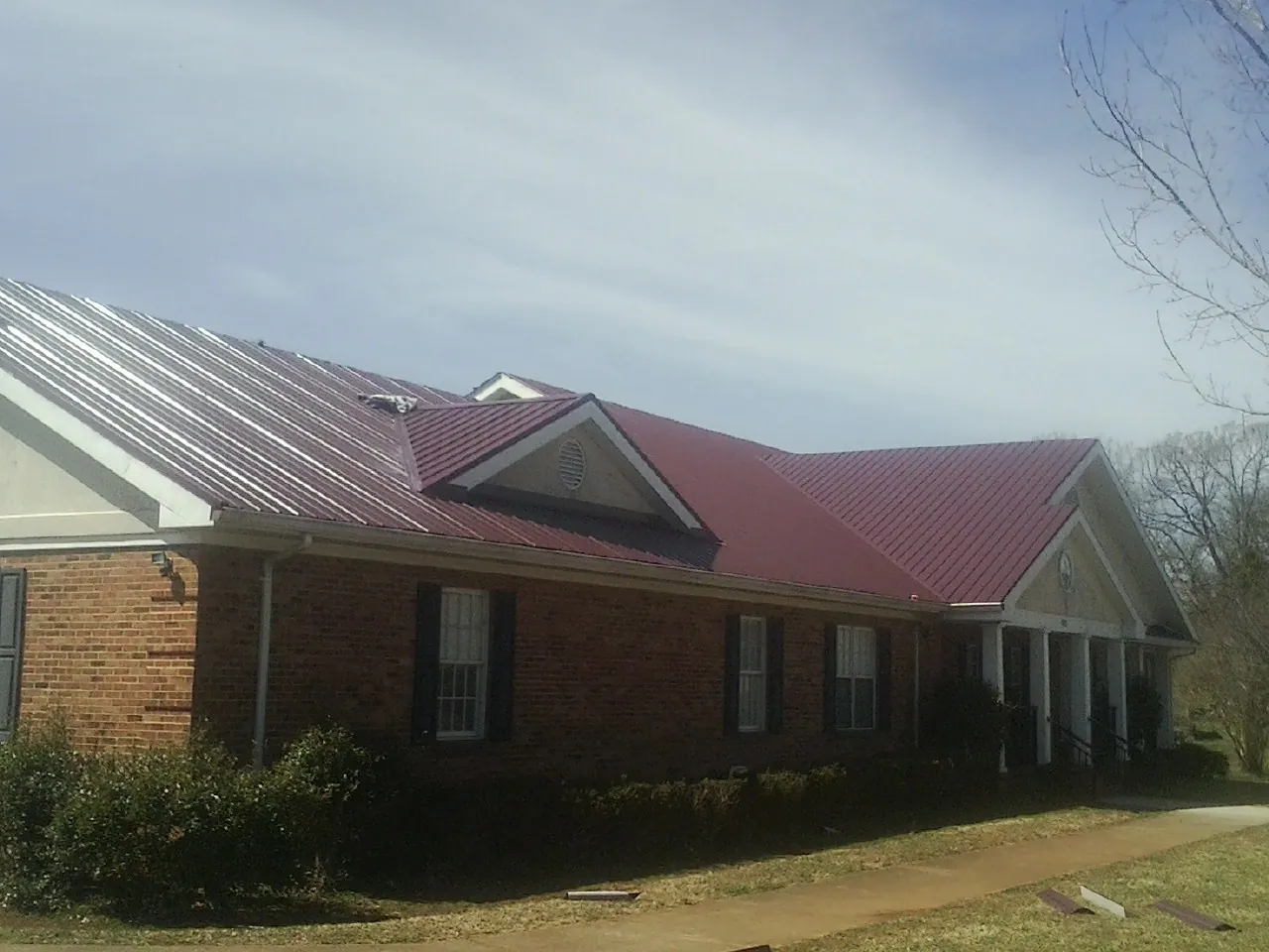 Red metal roof with gabled entries on a long brick building, from a Hail Damage Roof Repair job in Centreville
